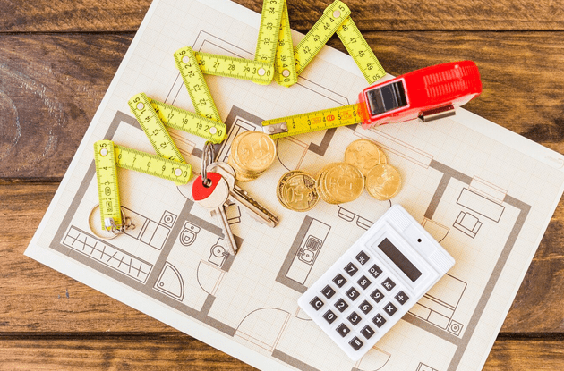 Elevated view of measure tape, stacked coins, key and calculator on blueprint for home improvement